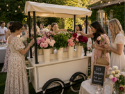 Vintage-style flower cart with women selecting bouquets at an outdoor event.